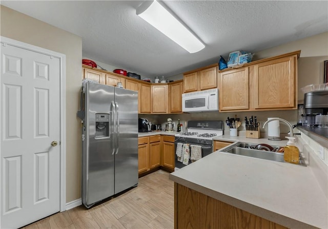 kitchen featuring sink, white appliances, kitchen peninsula, a textured ceiling, and light hardwood / wood-style flooring