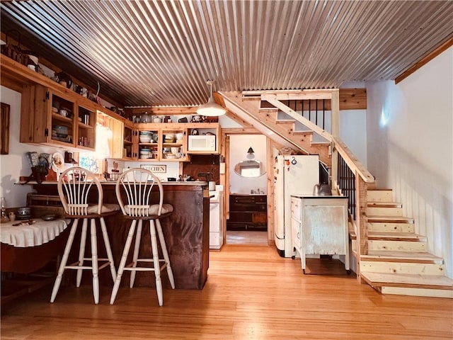 interior space featuring glass insert cabinets, light wood-style flooring, a kitchen breakfast bar, white appliances, and open shelves