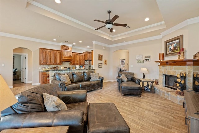 living room featuring light wood-type flooring, a raised ceiling, ceiling fan, and ornamental molding