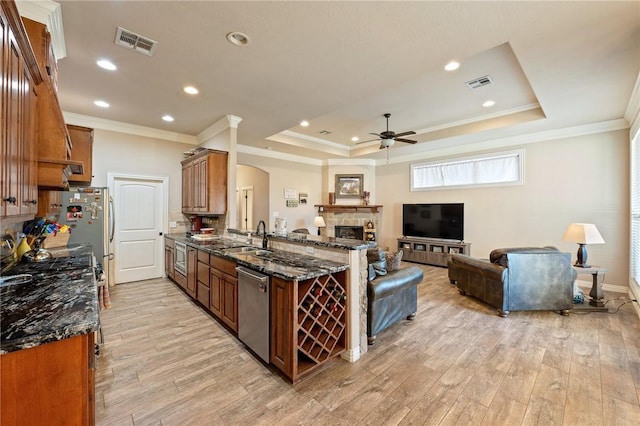 kitchen with kitchen peninsula, dark stone counters, light wood-type flooring, and appliances with stainless steel finishes