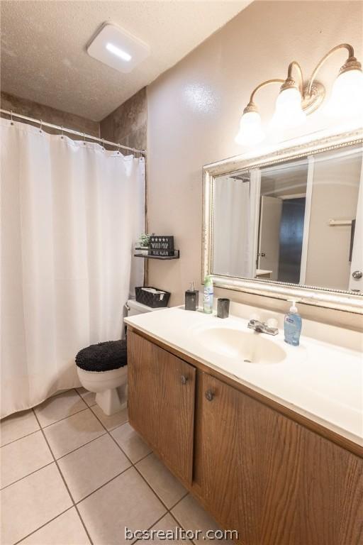 bathroom with tile patterned flooring, vanity, toilet, and a textured ceiling