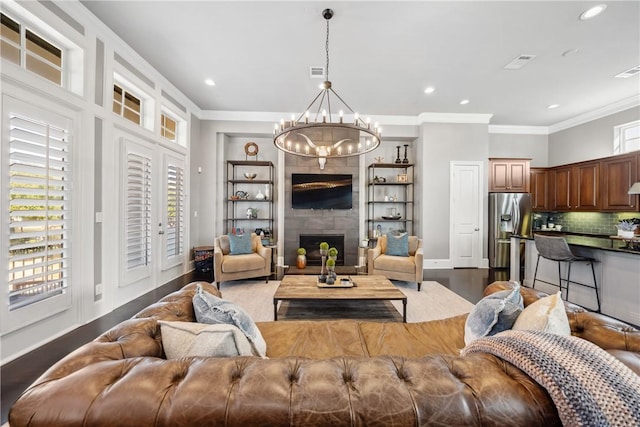 living area featuring a notable chandelier, a tiled fireplace, visible vents, and crown molding