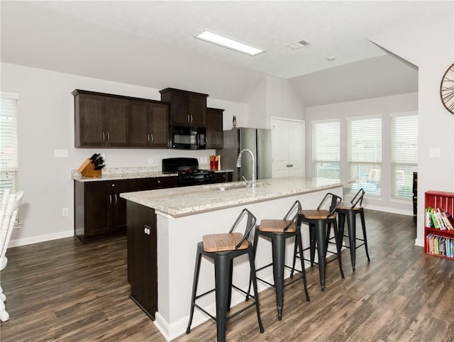 kitchen with dark brown cabinetry, a breakfast bar, dark wood-style floors, black appliances, and a kitchen island with sink