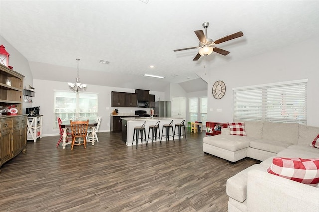 living area with vaulted ceiling, ceiling fan with notable chandelier, dark wood-style flooring, and a wealth of natural light