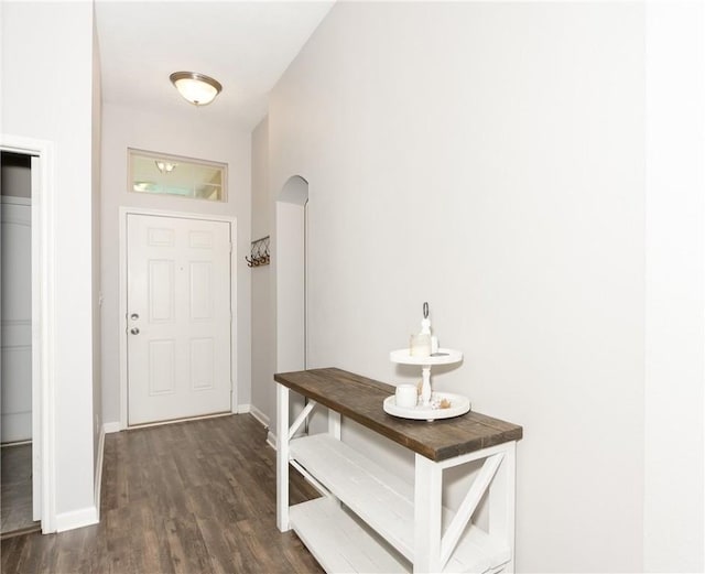 doorway featuring arched walkways, dark wood-type flooring, and baseboards