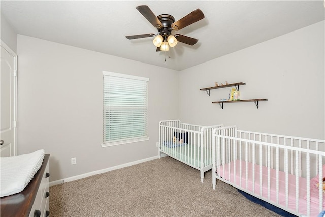 carpeted bedroom featuring a nursery area, a ceiling fan, and baseboards