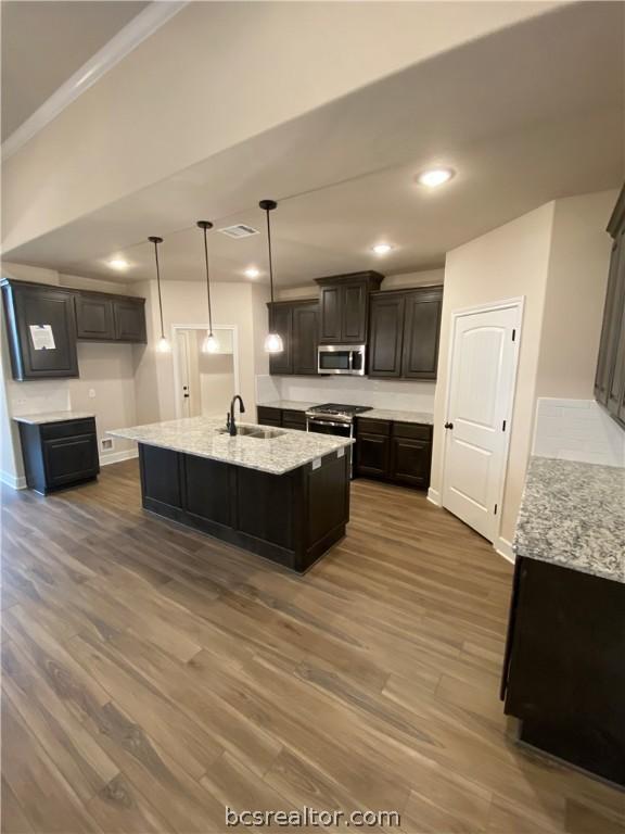 kitchen featuring decorative light fixtures, a center island with sink, stainless steel appliances, and dark hardwood / wood-style floors