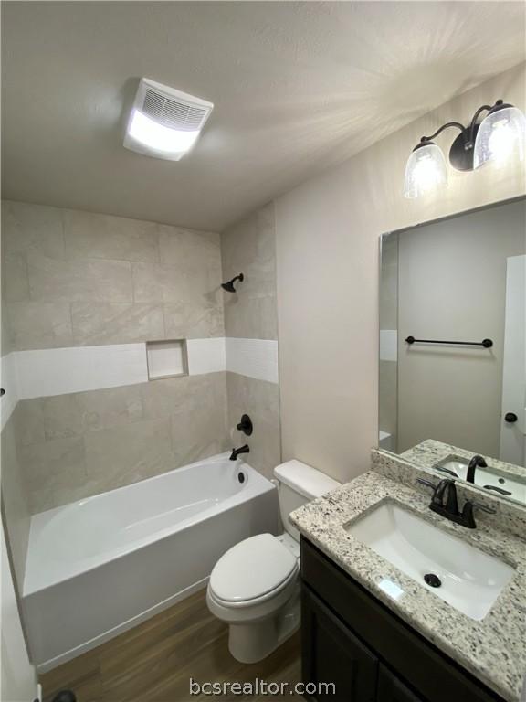 full bathroom featuring tiled shower / bath combo, toilet, wood-type flooring, and vanity