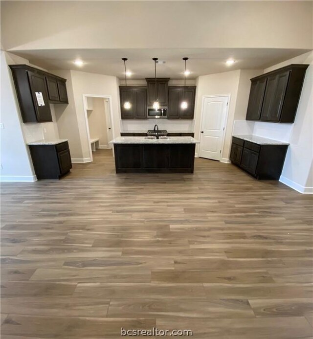 kitchen with sink, decorative light fixtures, hardwood / wood-style flooring, and an island with sink