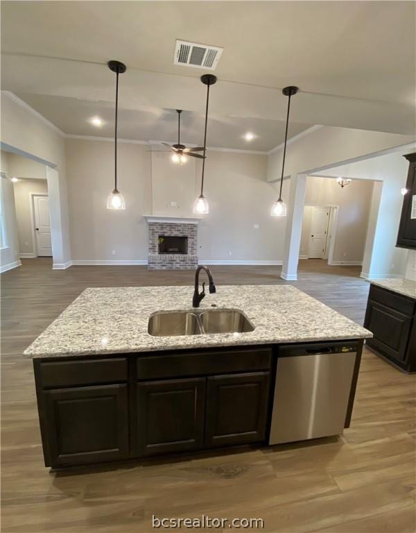 kitchen with a center island with sink, dishwasher, light stone countertops, and sink