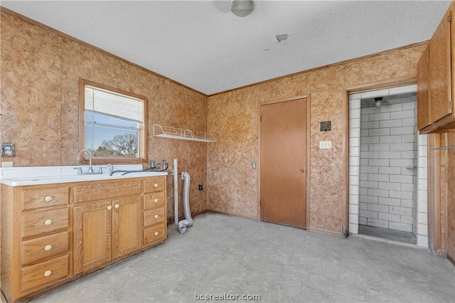 laundry room with cabinets, a textured ceiling, crown molding, and sink