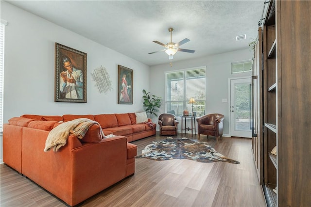 living room featuring ceiling fan, light wood-type flooring, and a textured ceiling