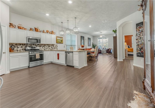 kitchen with hanging light fixtures, stainless steel appliances, kitchen peninsula, white cabinets, and hardwood / wood-style flooring