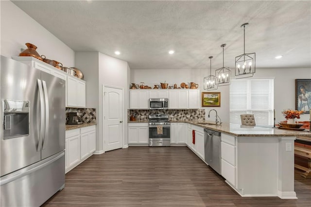 kitchen with a peninsula, stainless steel appliances, dark wood-style floors, white cabinetry, and a sink