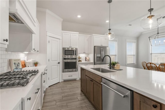 kitchen with sink, appliances with stainless steel finishes, hanging light fixtures, white cabinets, and wall chimney exhaust hood