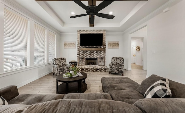 living room featuring ceiling fan, light hardwood / wood-style flooring, a fireplace, and a tray ceiling