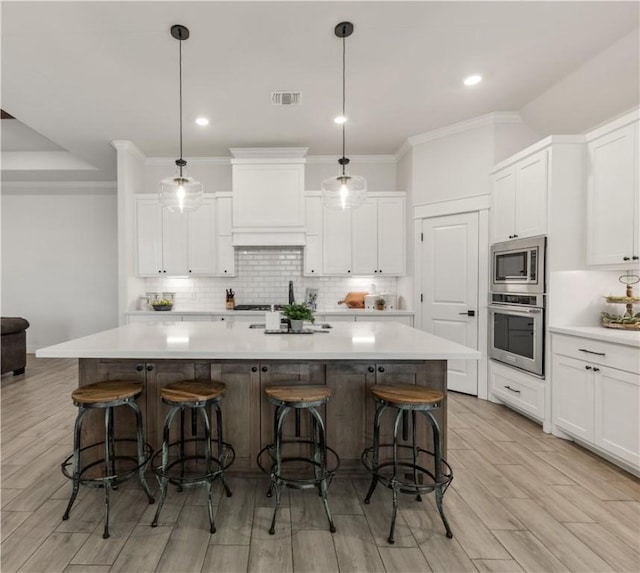 kitchen featuring a large island with sink, appliances with stainless steel finishes, and hanging light fixtures