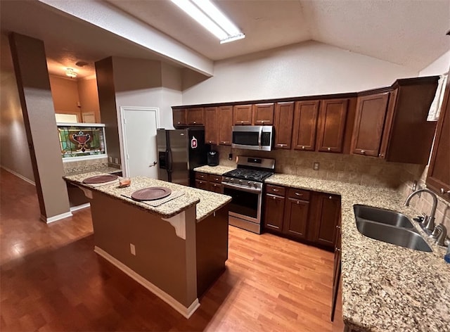 kitchen with light stone countertops, a center island, sink, stainless steel appliances, and vaulted ceiling