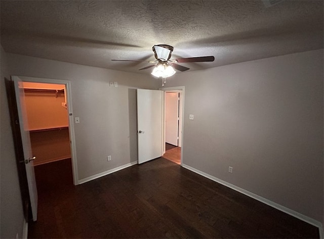 unfurnished bedroom with a textured ceiling, ceiling fan, dark wood-type flooring, a spacious closet, and a closet