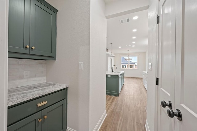 interior space featuring backsplash, pendant lighting, green cabinets, and light wood-type flooring