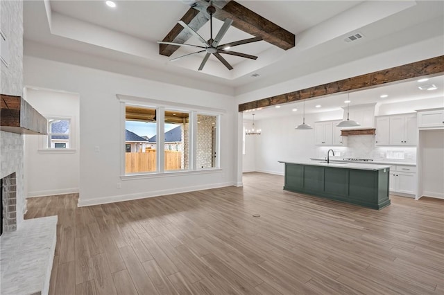 unfurnished living room featuring sink, ceiling fan with notable chandelier, beamed ceiling, and light hardwood / wood-style floors