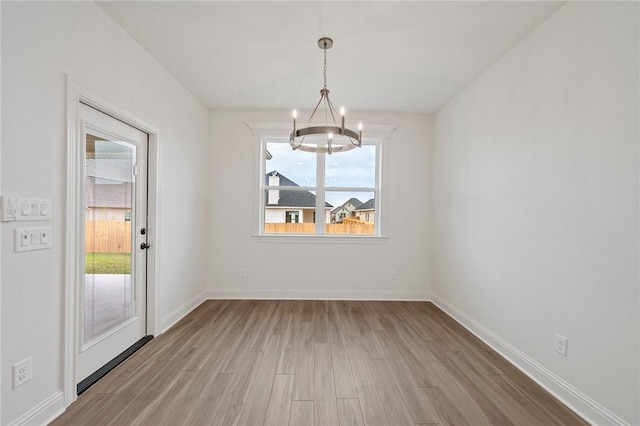 unfurnished dining area featuring light wood-type flooring, a chandelier, and plenty of natural light