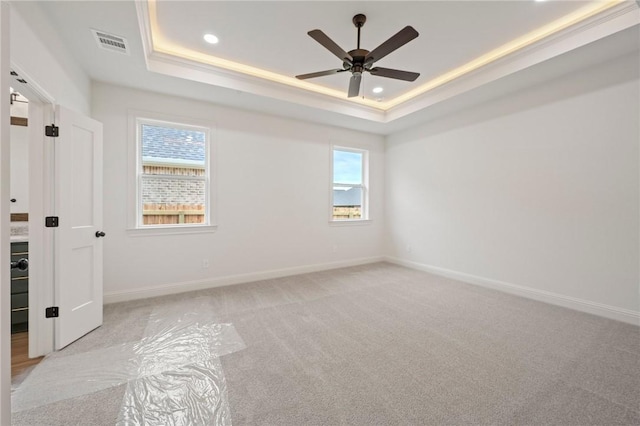 empty room featuring ceiling fan, light colored carpet, and a tray ceiling