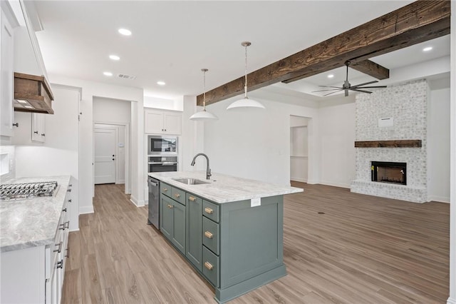 kitchen with white cabinets, sink, beam ceiling, stainless steel appliances, and a center island with sink