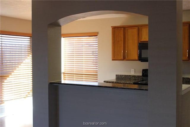 4031 Southern Trace Dr, College Station, TX 77845 - kitchen with black microwave, arched walkways, stove, and brown cabinetry