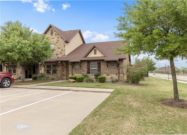 view of front of property with a shingled roof, uncovered parking, a front yard, and stone siding