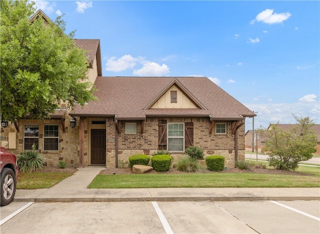 view of front of property featuring uncovered parking, stone siding, brick siding, and roof with shingles