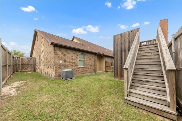 rear view of house with roof with shingles, a fenced backyard, brick siding, central AC, and a yard
