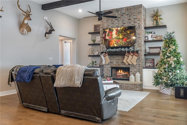 living room featuring ceiling fan, beamed ceiling, wood-type flooring, and a brick fireplace