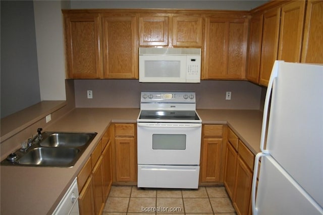 kitchen with a sink, light countertops, white appliances, brown cabinetry, and light tile patterned flooring
