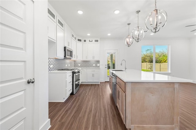 kitchen with sink, hanging light fixtures, a kitchen island with sink, white cabinets, and appliances with stainless steel finishes