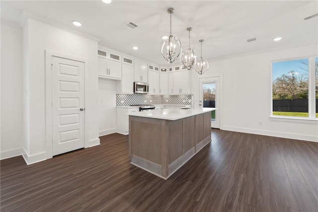 kitchen featuring white cabinets, a center island with sink, sink, hanging light fixtures, and tasteful backsplash