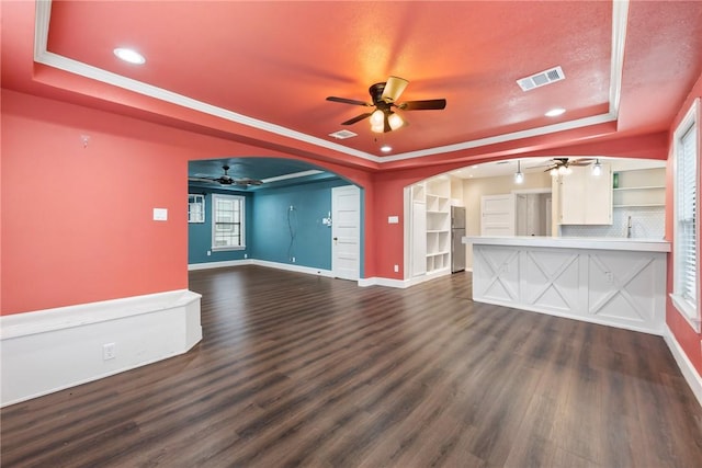 unfurnished living room featuring dark hardwood / wood-style flooring, built in features, crown molding, and a tray ceiling