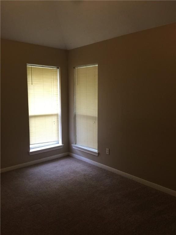 unfurnished room featuring dark colored carpet and baseboards