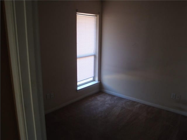 spare room with dark colored carpet and baseboards