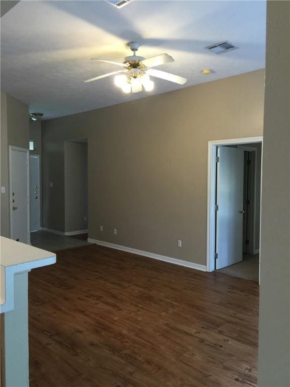 empty room with baseboards, visible vents, a ceiling fan, and dark wood-style flooring
