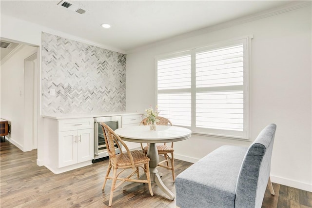 dining space featuring wine cooler, ornamental molding, and hardwood / wood-style flooring