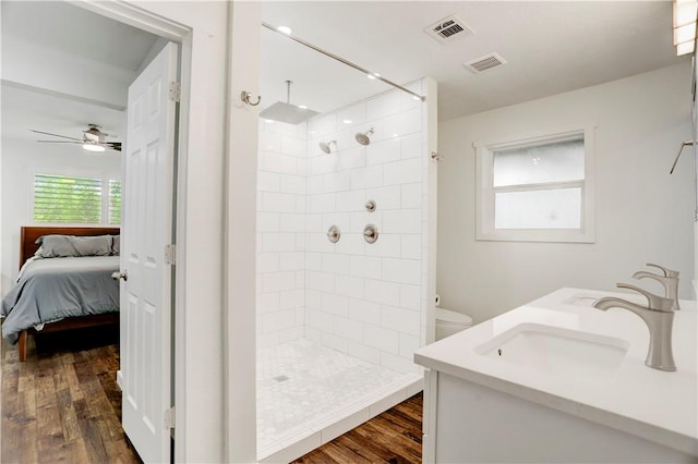 bathroom with hardwood / wood-style floors, ceiling fan, toilet, and tiled shower