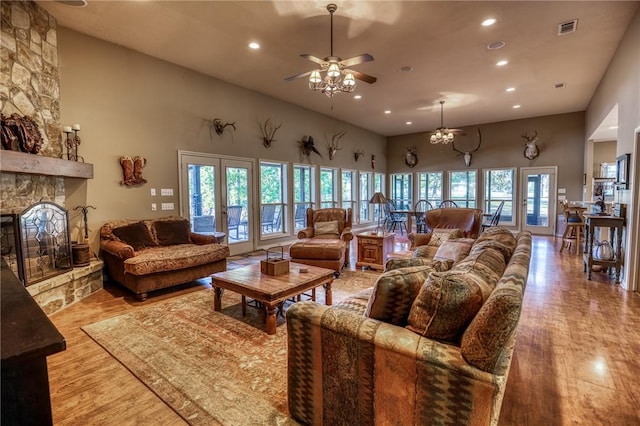 living room featuring french doors, a stone fireplace, light hardwood / wood-style flooring, ceiling fan, and a towering ceiling