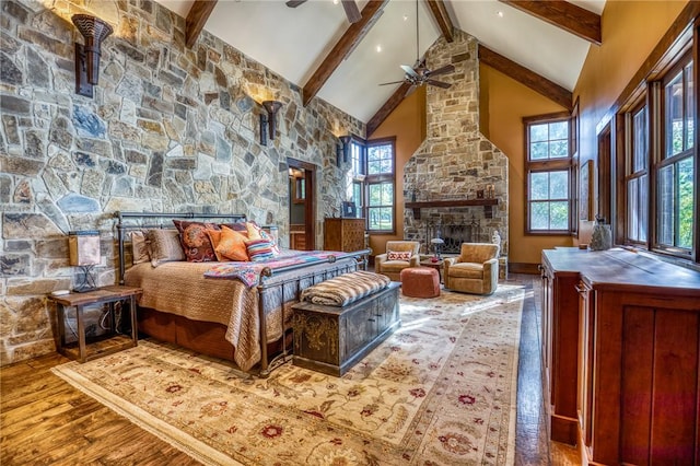 bedroom featuring beamed ceiling, a stone fireplace, hardwood / wood-style floors, and high vaulted ceiling