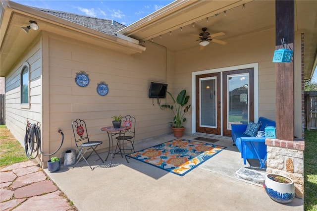 view of exterior entry with a patio area, ceiling fan, and roof with shingles