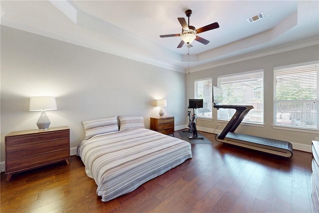 bedroom with a raised ceiling, wood finished floors, baseboards, crown molding, and a ceiling fan
