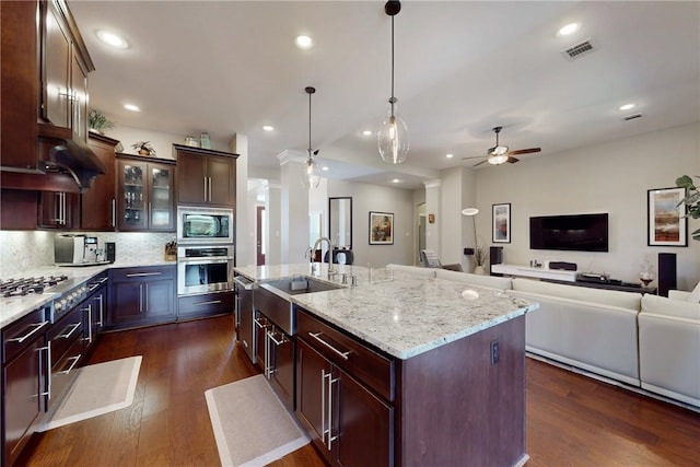 kitchen featuring a sink, appliances with stainless steel finishes, a ceiling fan, an island with sink, and dark wood-type flooring