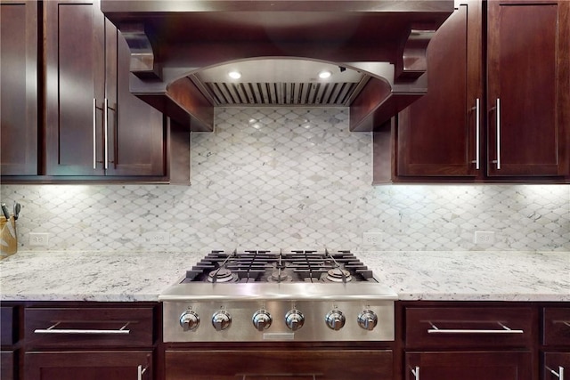 kitchen with stainless steel gas stovetop, custom exhaust hood, decorative backsplash, and light stone countertops