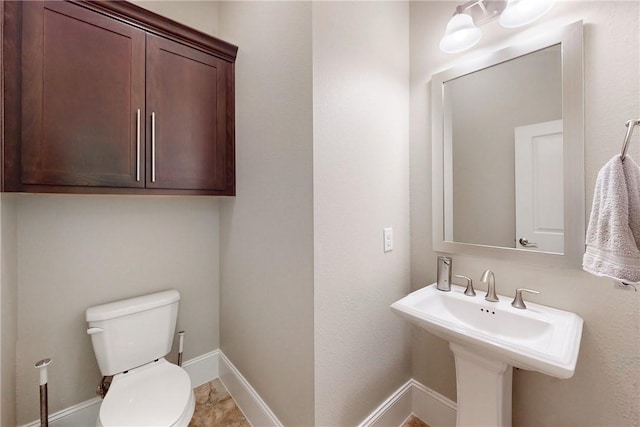 half bathroom with toilet, baseboards, and a sink