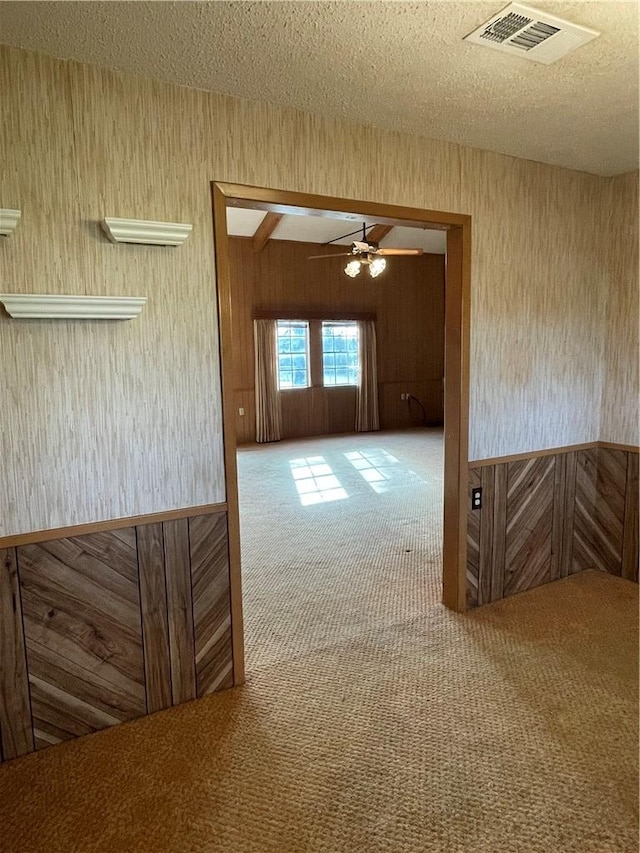 carpeted spare room featuring a ceiling fan, wooden walls, visible vents, and a textured ceiling